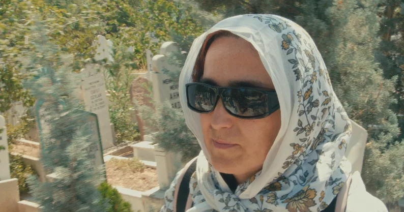 Nahaufnahme einer Frau mit Kopftuch und Sonnenbrille auf einem Friedhof