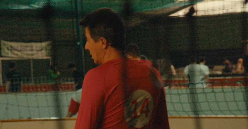 Mann im roten Trikot von hinten am Rand eines Spielfelds